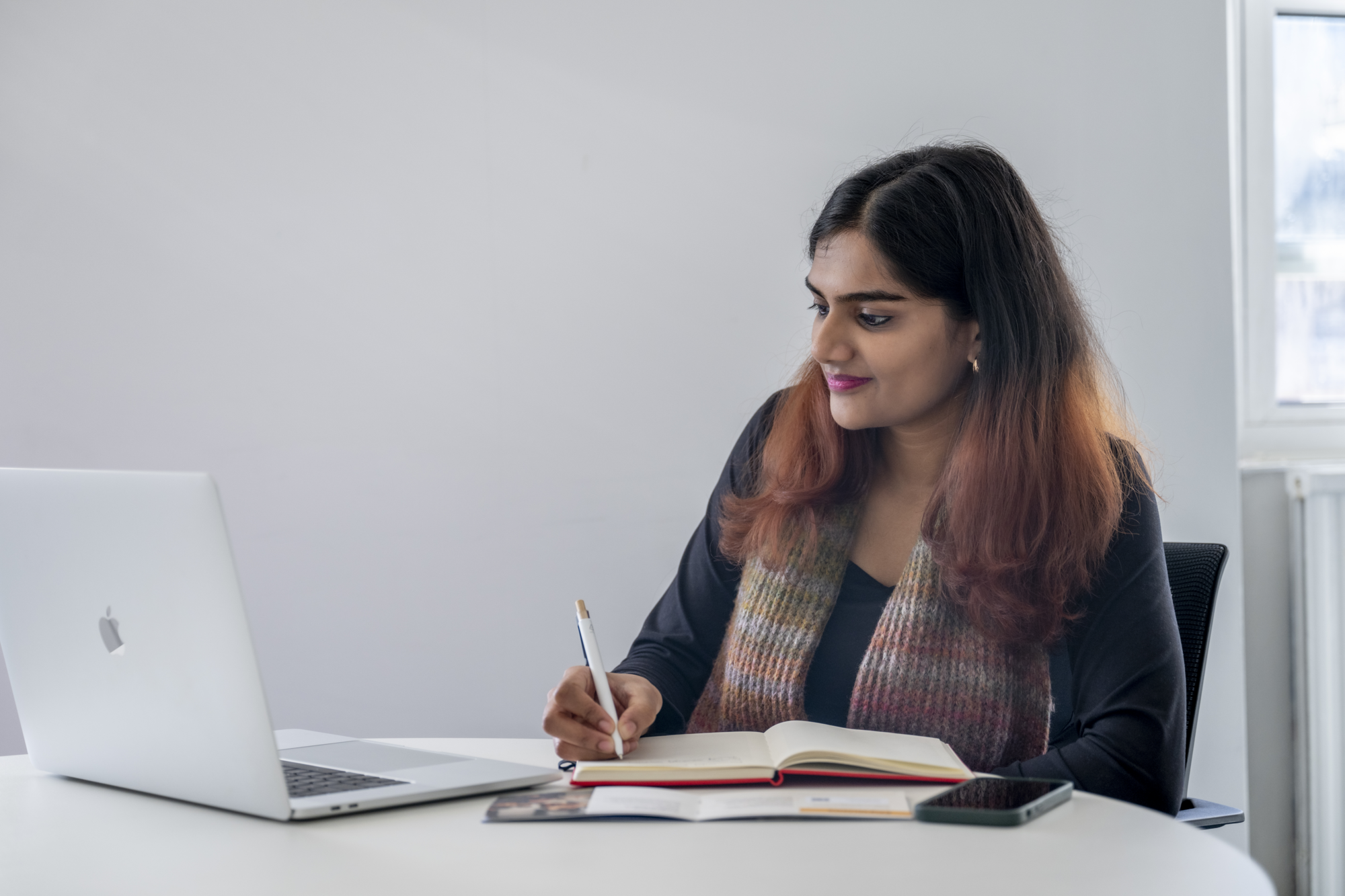A woman smiling at a laptop taking notes